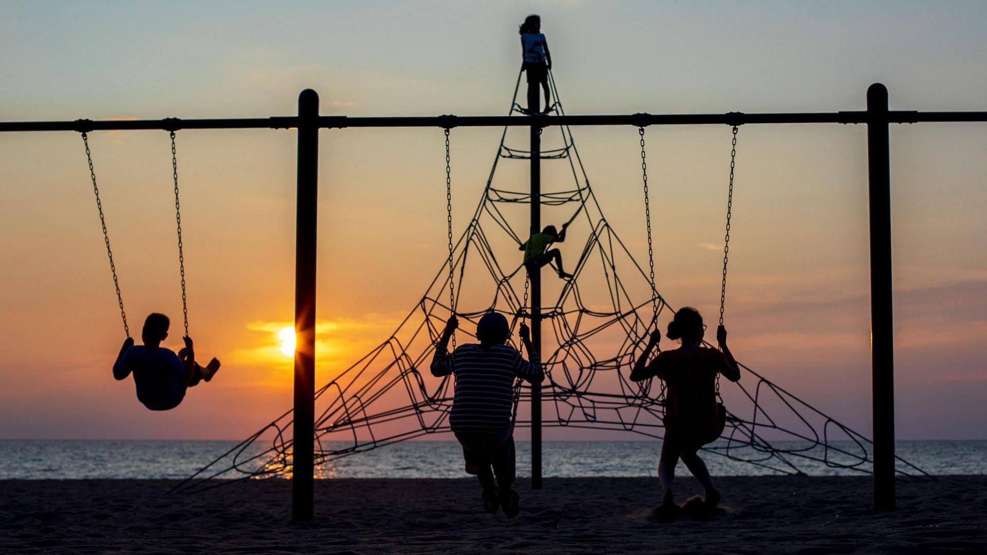 Kids playing on toys at the beach at sunset.